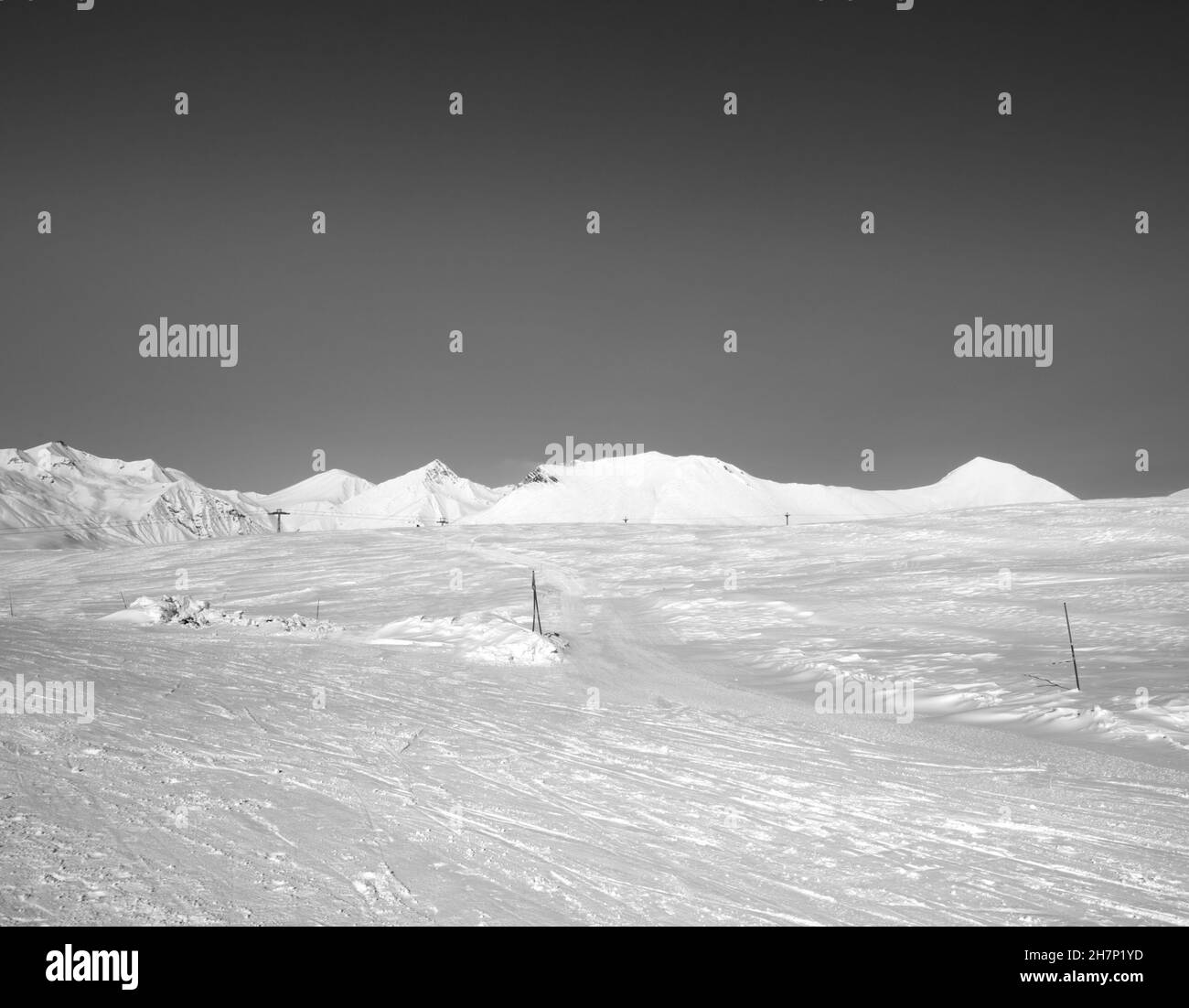 Pista de esquí nevada con huellas de esquís y snowboards al sol el día de invierno. Montañas del Cáucaso, Georgia, región Gudauri. Paisaje en blanco y negro. Foto de stock