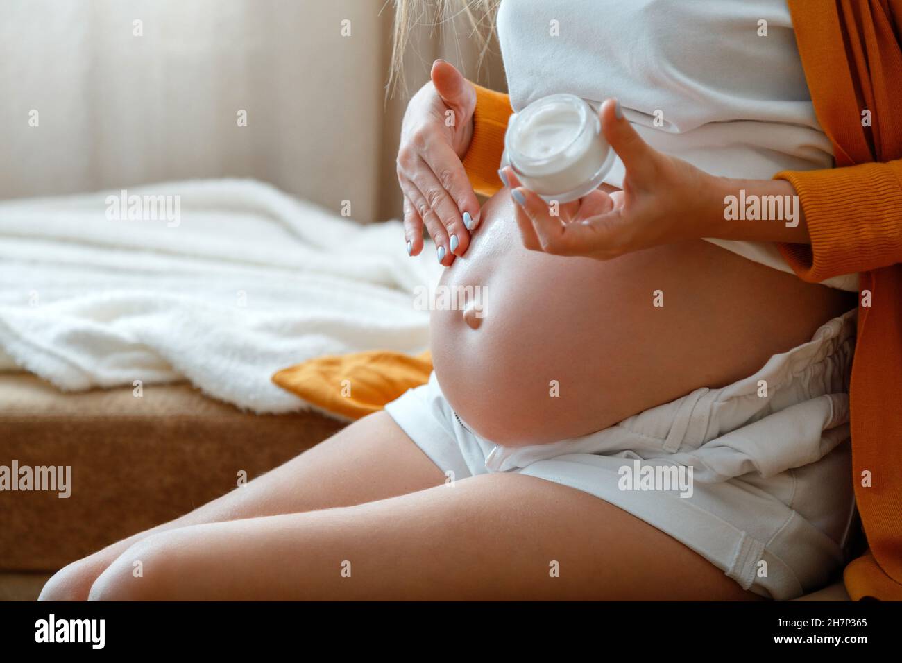 La mujer embarazada le da un olor a crema en el vientre de su casa. Atención de la salud durante la maternidad y el embarazo. Cuidado diario de la piel del bebé embarazada. Irreconocible Foto de stock