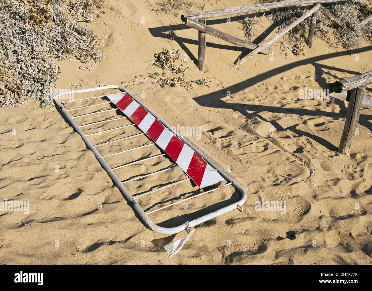 barrera metálica que cierra un camino que conduce a la playa tumbada en la arena Foto de stock