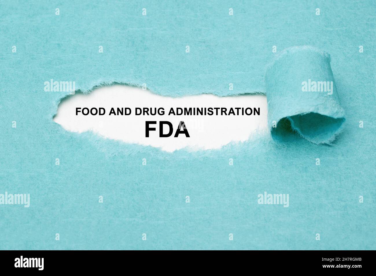 Texto impreso FDA Food and Drug Administration que aparece detrás de papel azul rasgado. Foto de stock