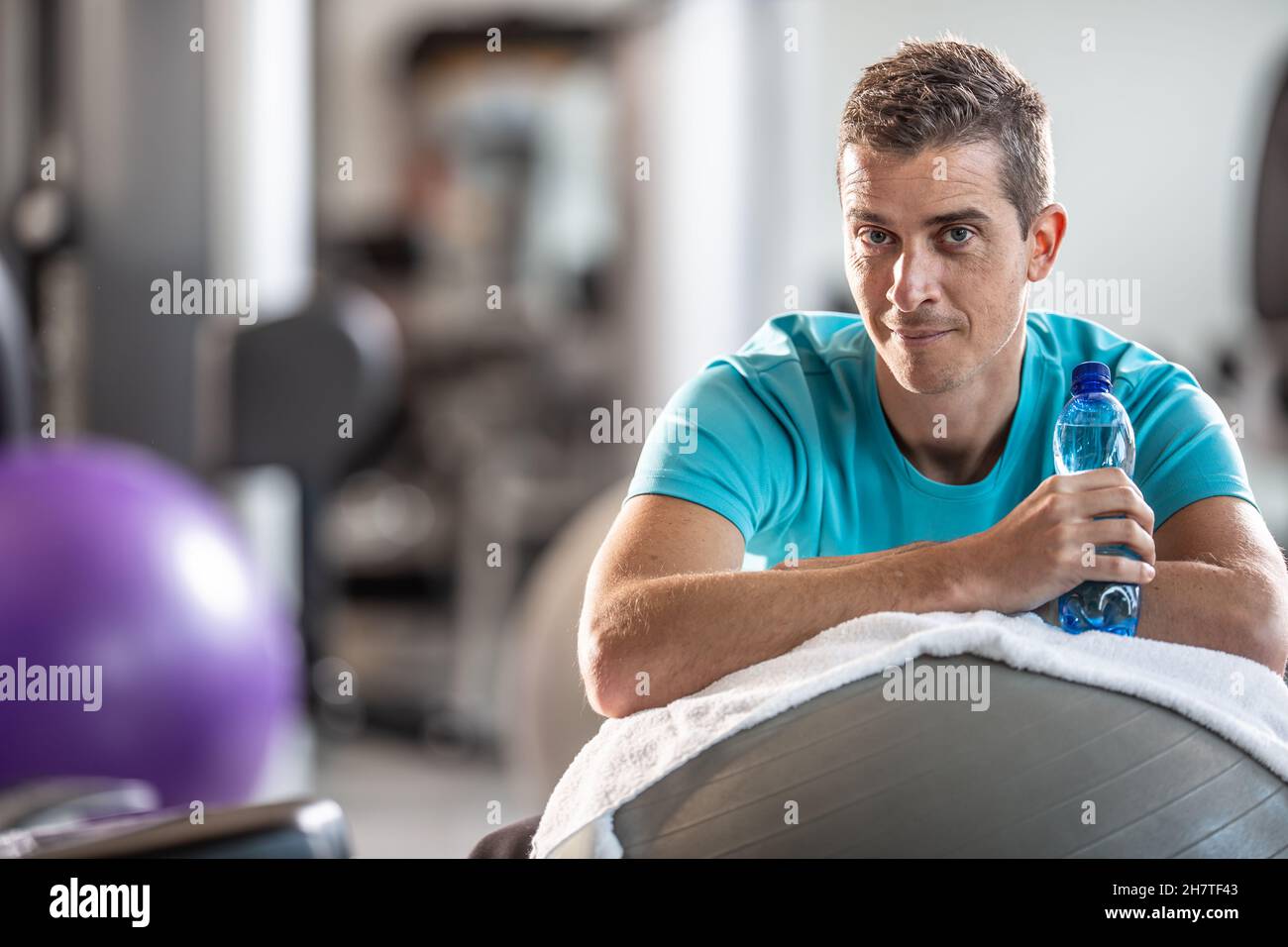 Hombre sosteniendo la botella de agua descansa dentro del gimnasio durante una sesión de entrenamiento. Foto de stock