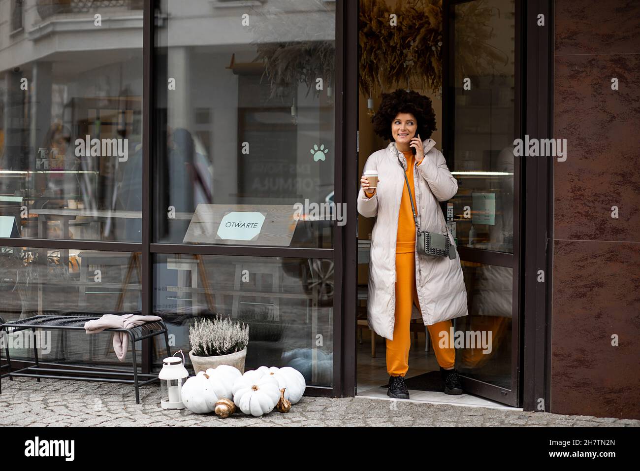 Mujer joven caucásica. Estilo de pelo Afro. Sport Sportswear. Caminando por  la calle europea, saliendo de la cafetería, sosteniendo una taza de café o  té. Vida urbana, estilo de calle Fotografía de