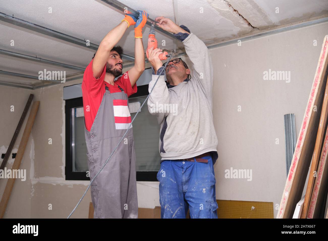 Dos trabajadores que ensamblan un marco de metal de techo suspendido con un destornillador. Foto de stock