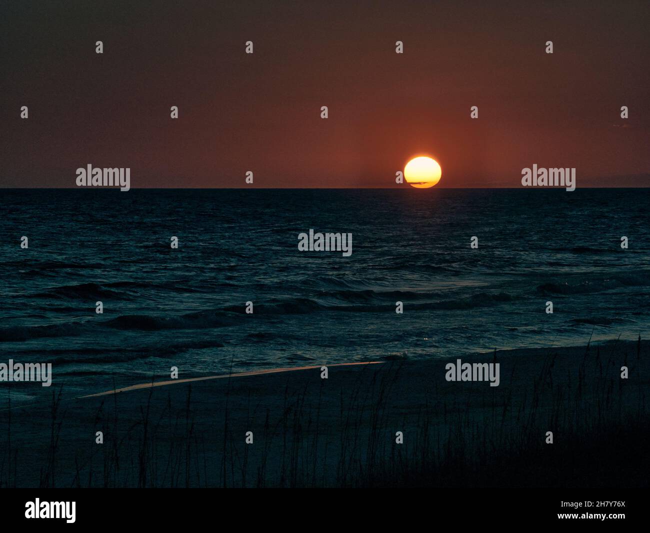 Moody Sunset sobre el océano o el Golfo de México con una gran bola naranja justo sobre el horizonte. Foto de stock