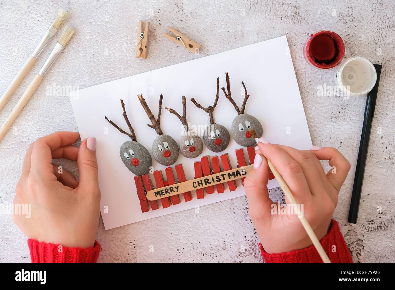 Briy Feliz venado de Navidad en tarjeta de felicitación tarjeta postal  hecha de guijarros, piedras de mar, clothespins y ramas sobre fondo blanco.  bricolaje de estilo ecológico natural Fotografía de stock -