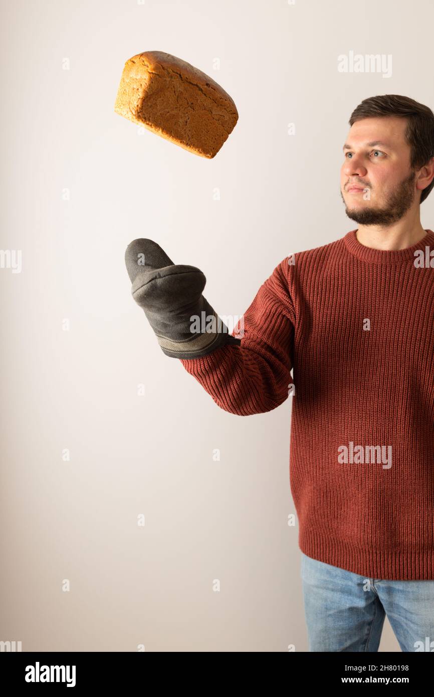 Un hombre en un suéter lanza una hogaza de pan de centeno al aire. Vista frontal. Vertical. Foto de stock