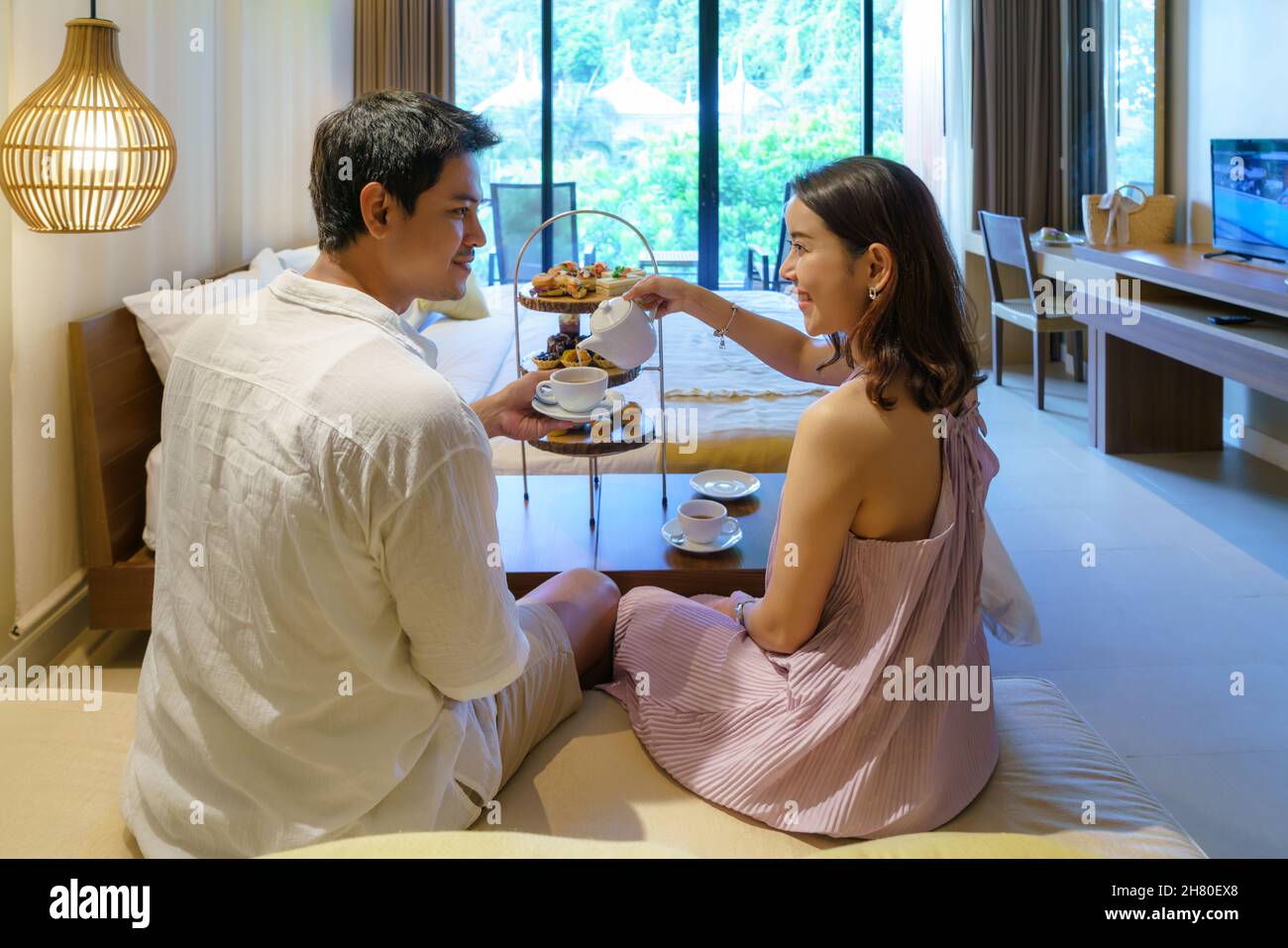 Las parejas asiáticas disfrutan de unas vacaciones románticas. Tomando un té de la tarde como una mujer vierte té para su novio en un lujoso dormitorio de hotel. Foto de stock