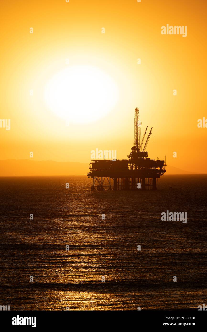 Plataforma petrolífera frente a la costa de California contra un cielo de color naranja y malhumorado cuando el sol se pone detrás de la plataforma. Foto de stock