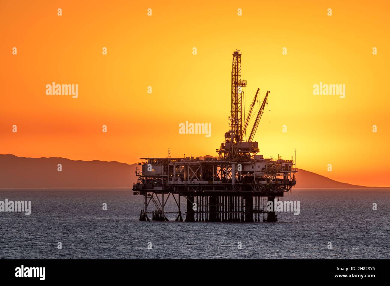 La plataforma petrolífera offshore frente a la costa de California se enmarca contra un cielo naranja lleno de humo de un incendio cercano mientras el sol se pone detrás de la plataforma. Foto de stock