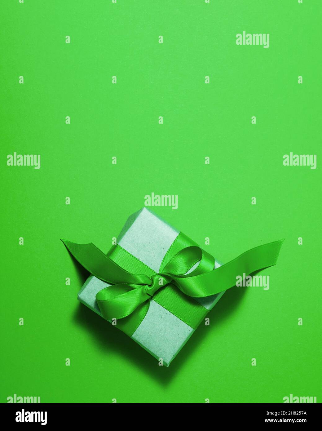 Caja de regalo de papel marrón con lazo verde satinado en la parte superior sobre fondo verde. Navidad madre y padre San Valentín días y cumpleaños presen Foto de stock