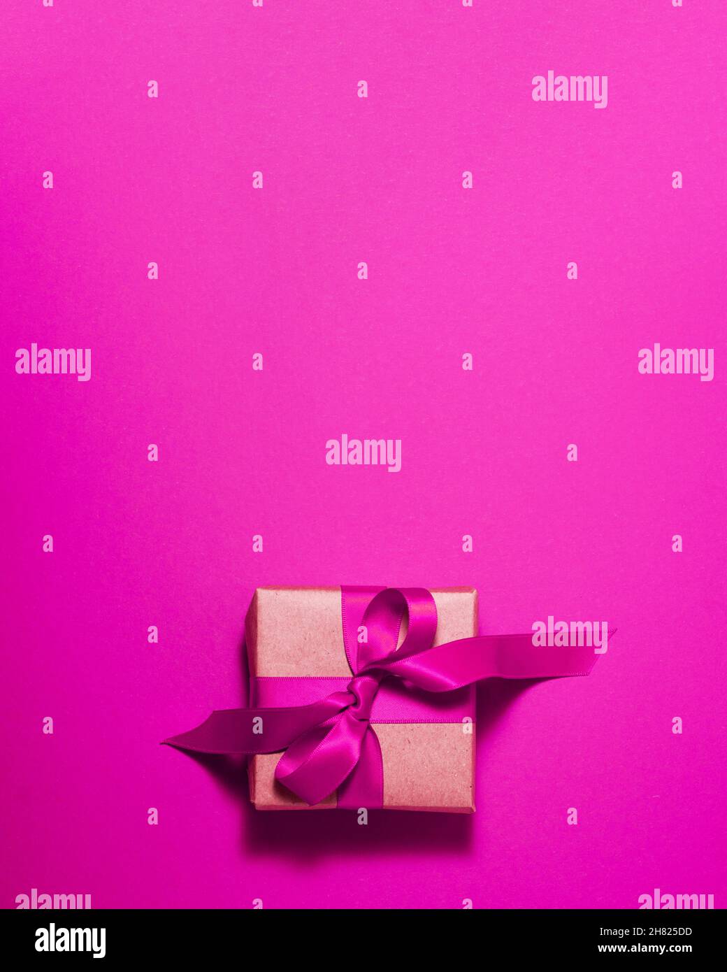 Caja de regalo de papel marrón con lazo de satén púrpura en la parte superior sobre fondo morado. Vacaciones de Navidad madre y padre Días de San Valentín y pres de cumpleaños Foto de stock