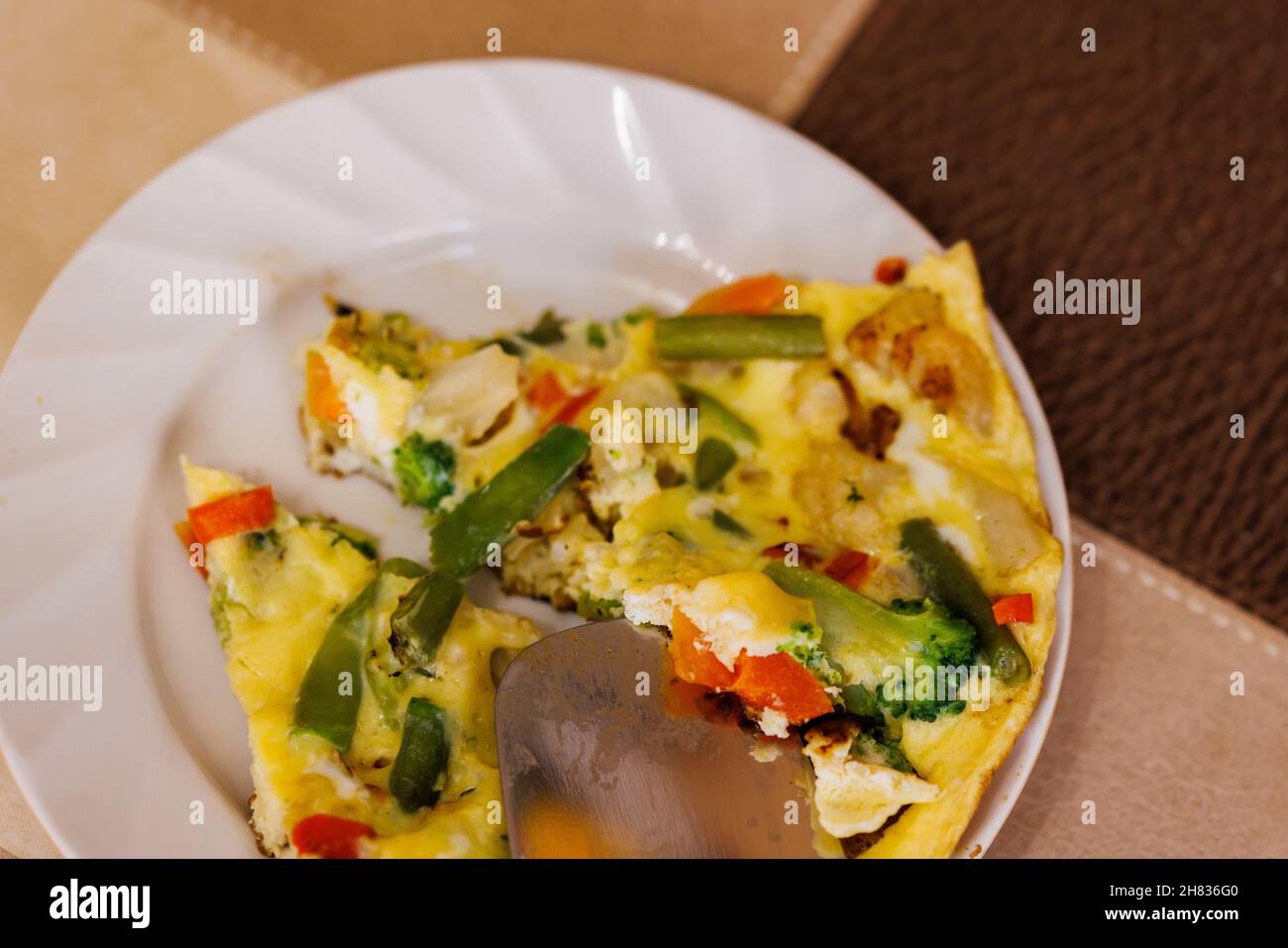 plato con rodajas de tortilla de huevos revueltos con verduras y espátula de acero inoxidable Foto de stock