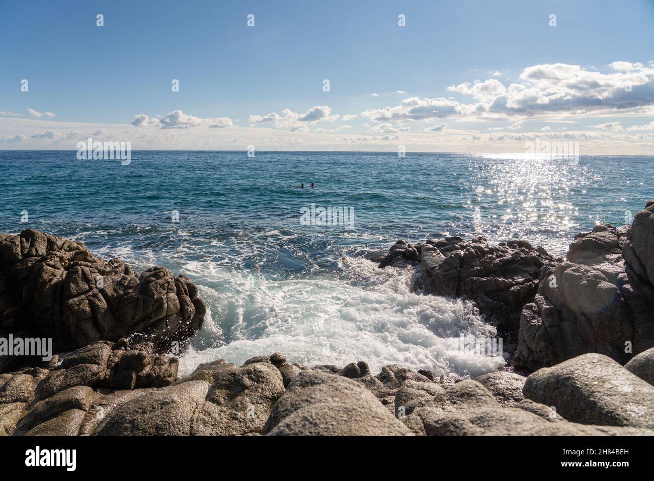las olas salpican la roca en la orilla del mar, un mar bastante tranquilo con cielo azul y algunas nubes Foto de stock