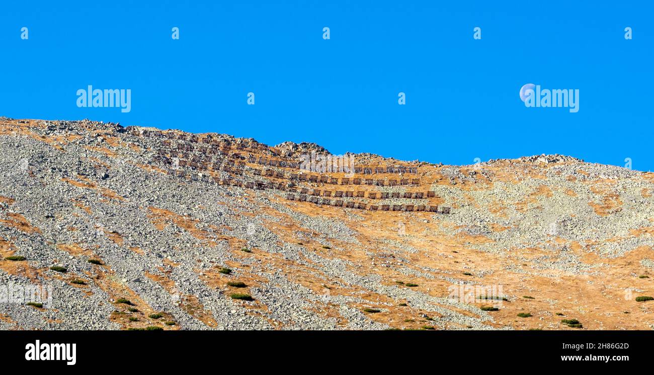 Protección de avalanchas o barrera en el paso de montaña Lomnicke sedlo en Tatras altos con luna en el cielo azul. Eslovaquia. Foto de stock