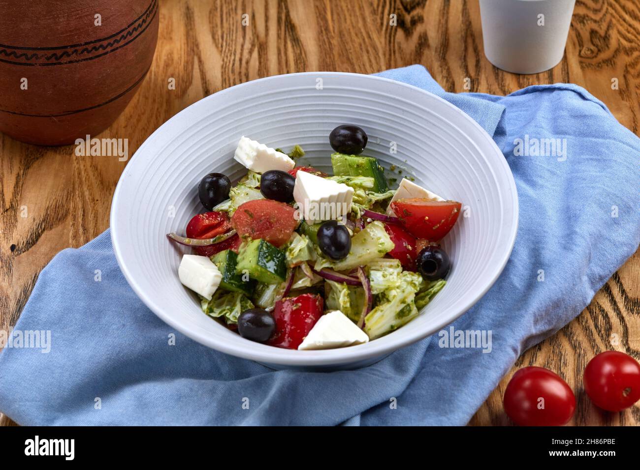 Tazón de ensalada griego con queso Feta, tomates y aceitunas sobre fondo de madera rústica Foto de stock