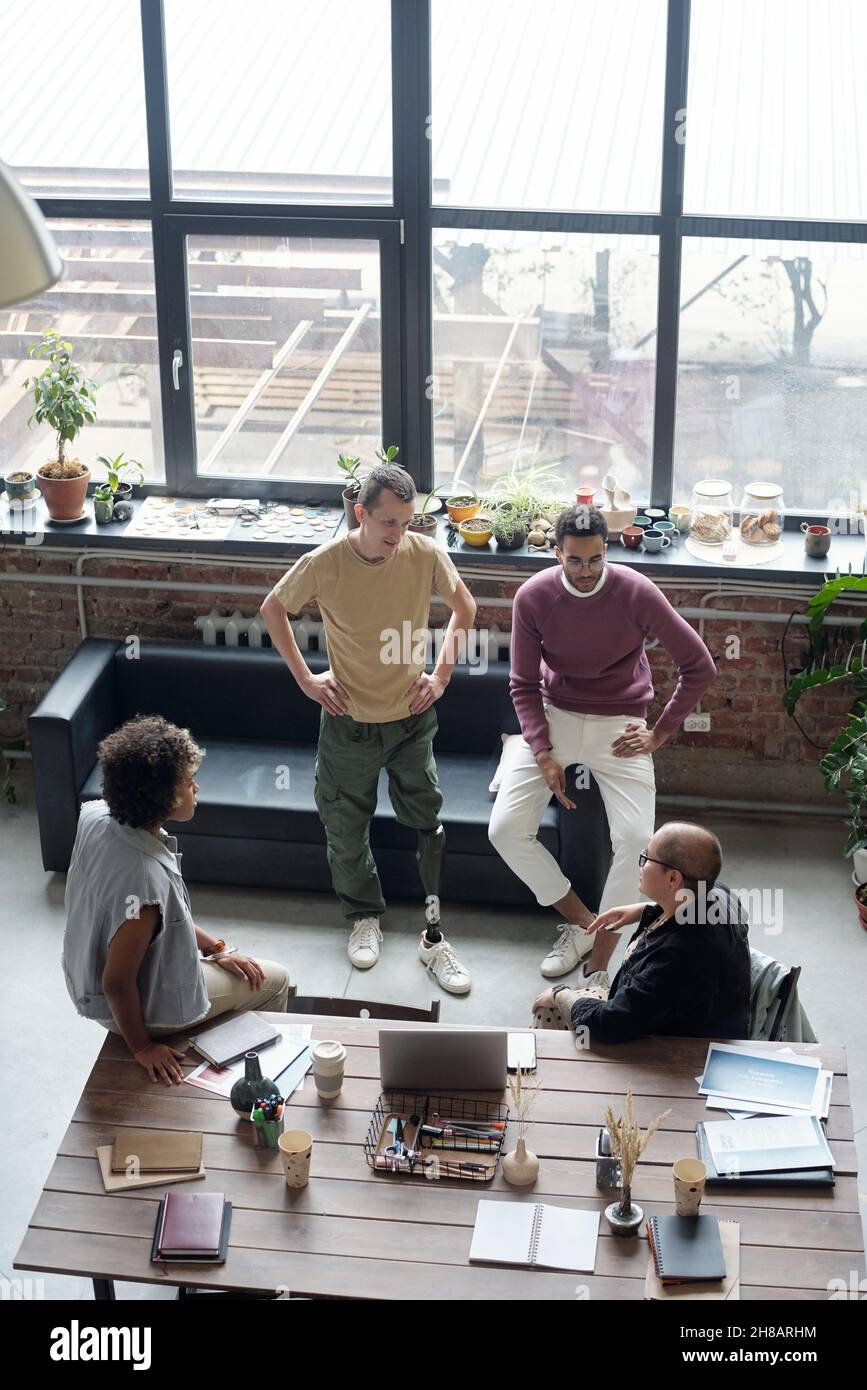 Grupo de jóvenes compañeros de trabajo en ropa de trabajo que discuten ideas para un nuevo proyecto de negocio en una reunión en una oficina grande Foto de stock