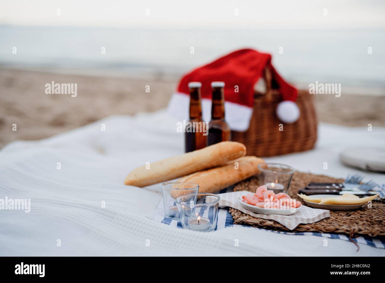 Picnic en la playa con camarones, cerveza, velas y sombrero de santa. Año nuevo exótico y Navidad Foto de stock