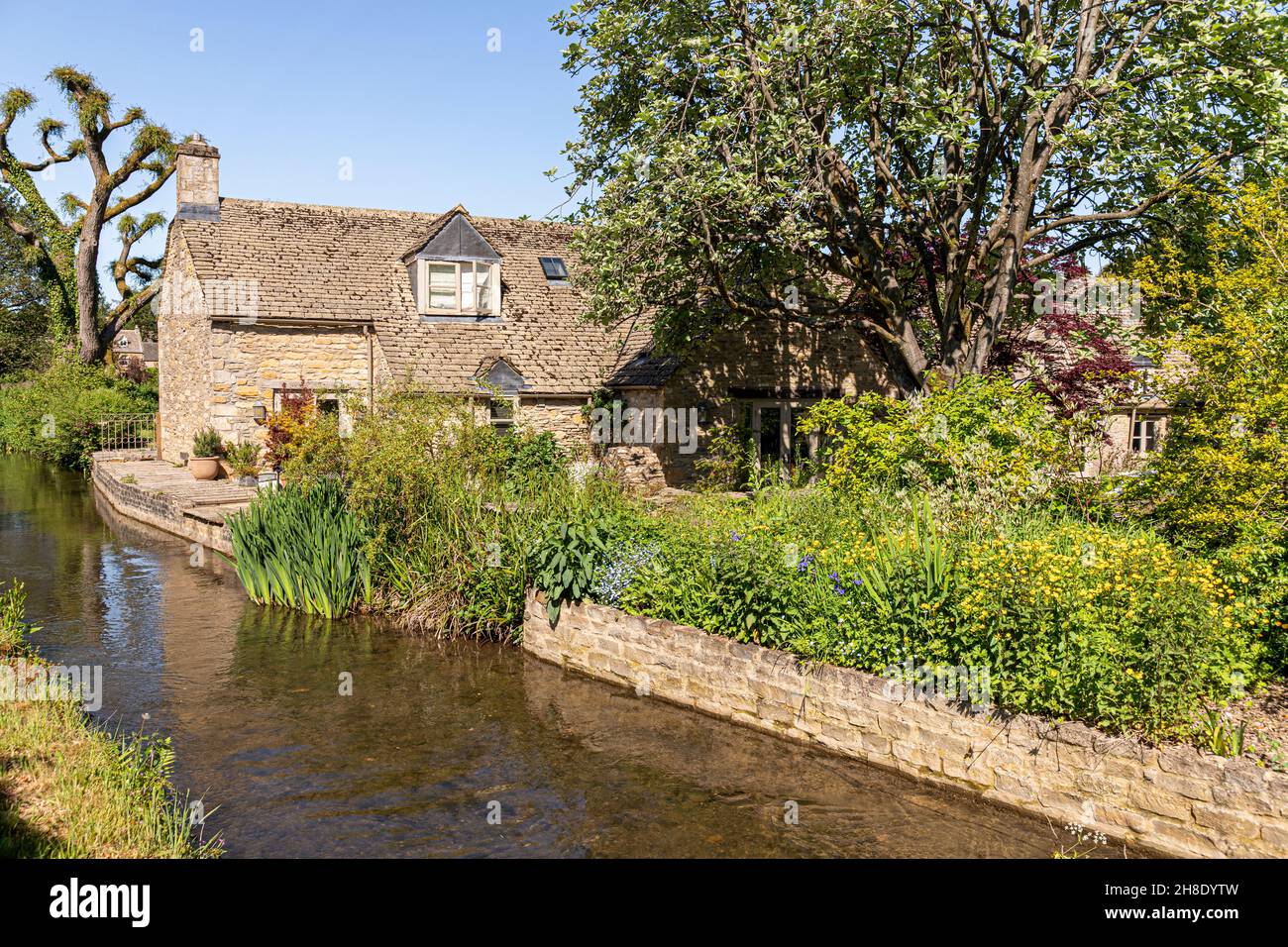 Una tradicional casa de piedra junto al río Windrush, que fluye a través de la aldea Cotswold de Naunton, Gloucestershire Reino Unido Foto de stock