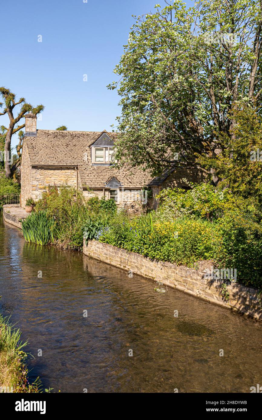 Una tradicional casa de piedra junto al río Windrush, que fluye a través de la aldea Cotswold de Naunton, Gloucestershire Reino Unido Foto de stock