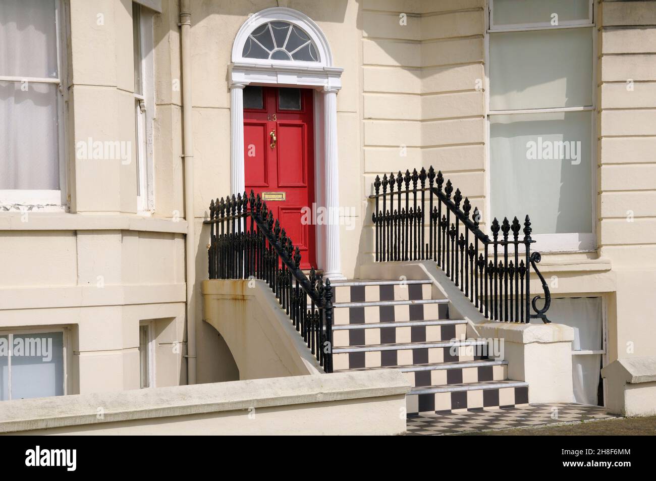 Exterior de la propiedad con una puerta roja, barandillas de hierro forjado y escalones blancos y negros, Brighton, East Sussex, Inglaterra, Reino Unido Foto de stock