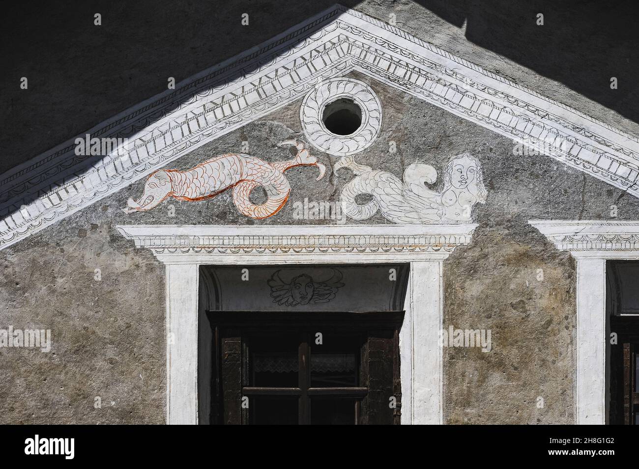 Una sirena buxom se recuesta por encima de una ventana junto a un monstruo marino escamoso con una cola con puntas de flecha y una llamativa lengua de arte rústico sgraffito en una casa familiar tradicional restaurada en Ardez, Graubünden o el cantón de Grisons, en el este de Suiza. Dragones, sirenas y criaturas marinas se encuentran en muchas viviendas en la zona restaurada por artistas locales de sgraffito a principios de 1900s. Foto de stock