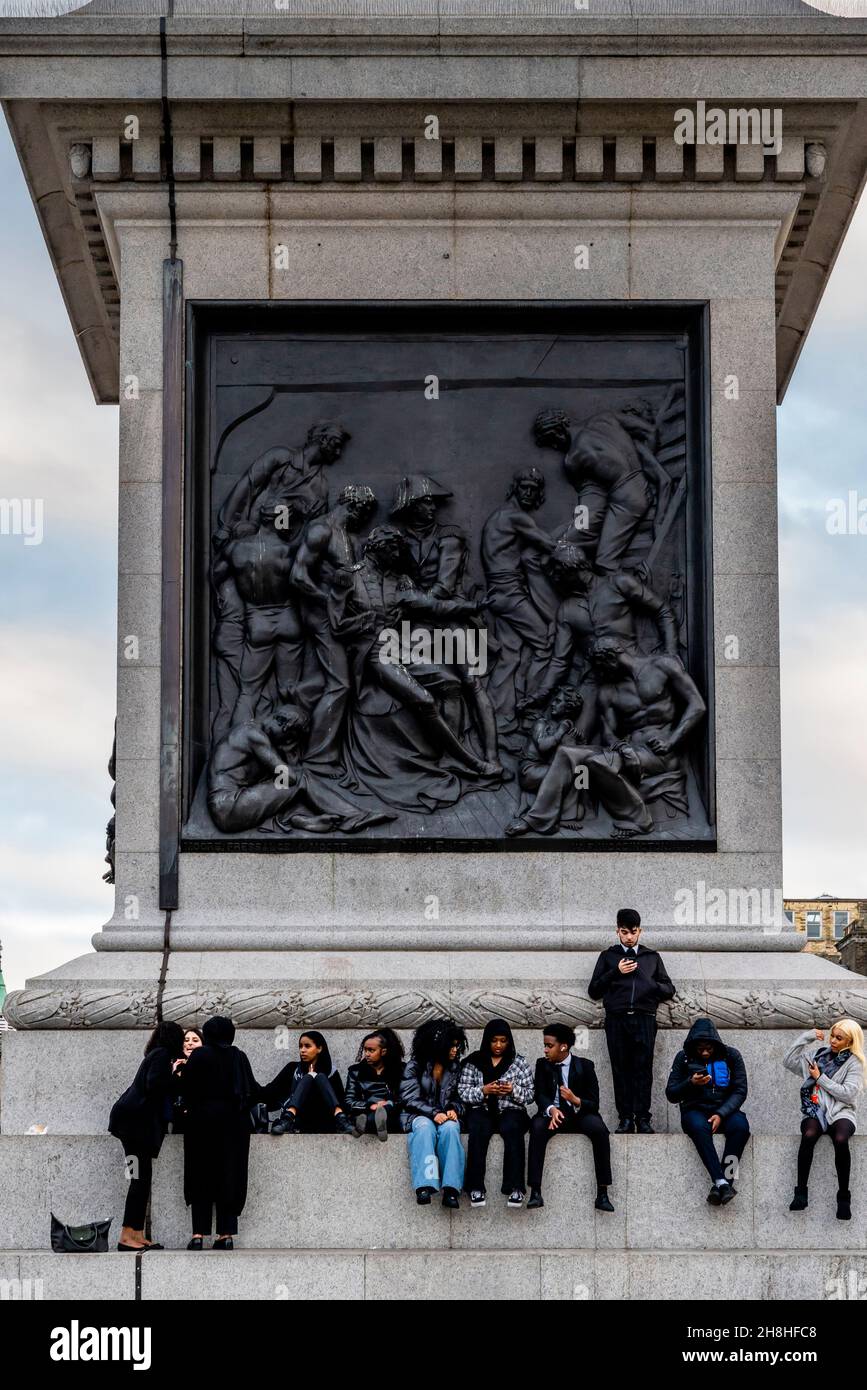 Un grupo multiétnico de jóvenes sentados en los escalones de la columna de Nelson, Trafalgar Square, Londres, Reino Unido. Foto de stock