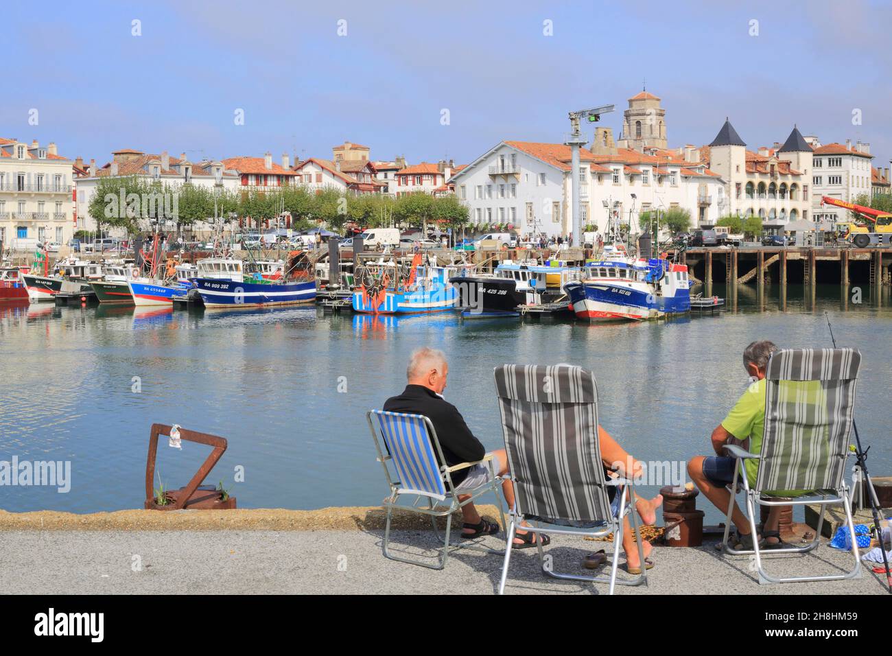 Francia, Pirineos Atlánticos, País Vasco, San Juan de Luz, pescadores aficionados en el puerto pesquero con la plaza Luis XIV en el fondo a la izquierda Foto de stock