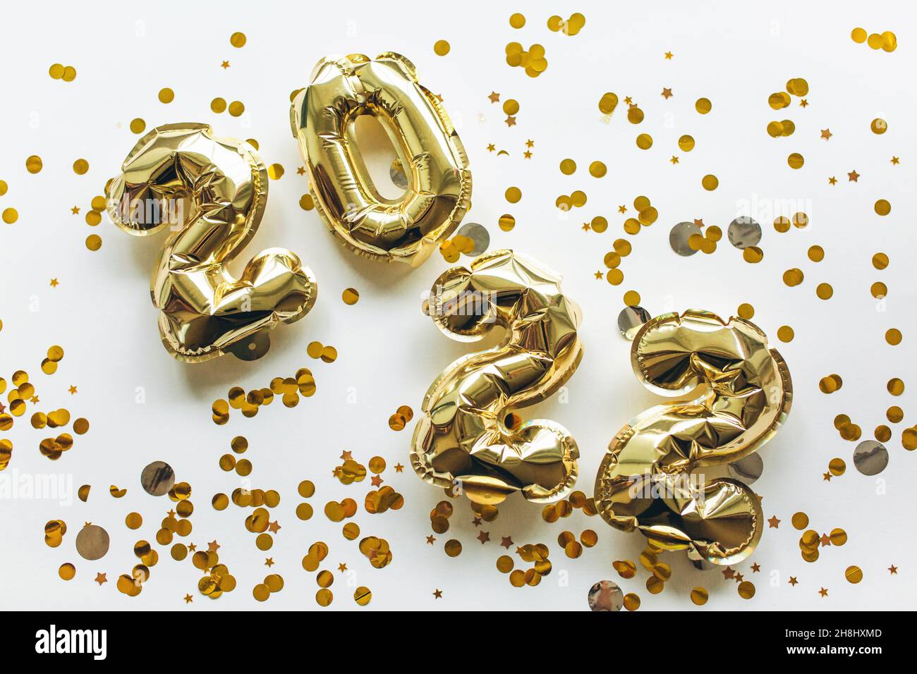 Globos hechos de papel de aluminio dorado con los números 2022 sobre fondo blanco con lentejuelas de oro. Celebración de Navidad, Año Nuevo y el concepto de vacaciones. Plano, vista superior. Foto de stock