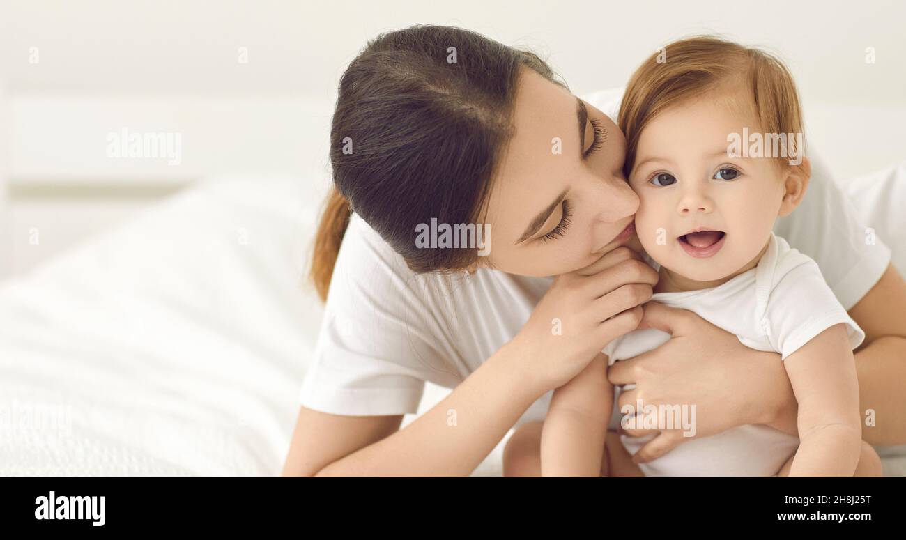 Bandera con una mamá feliz besando a su linda niña mientras acurruca en una cama juntos Foto de stock