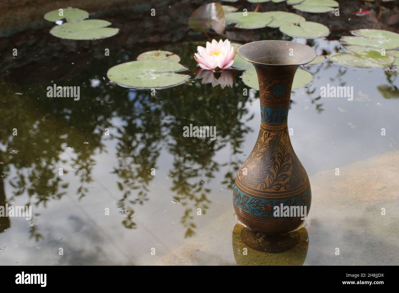 Antiguo jarrón de cobre indio en el lago con nenúfares Foto de stock