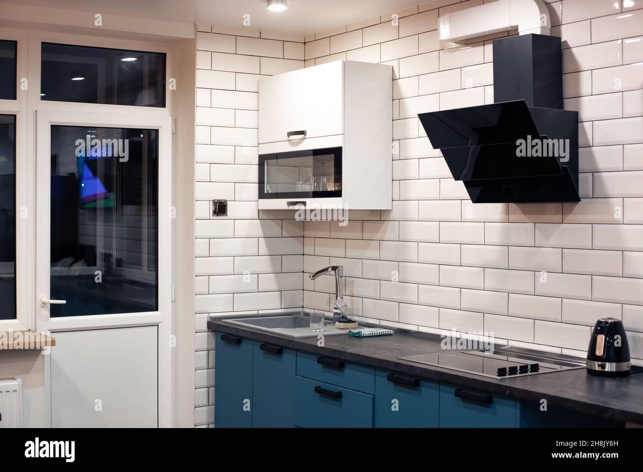 Cocina interior. Las paredes están cubiertas con azulejos en forma de  ladrillo blanco, muebles de cocina azul y blanco y electrodomésticos negros  Fotografía de stock - Alamy