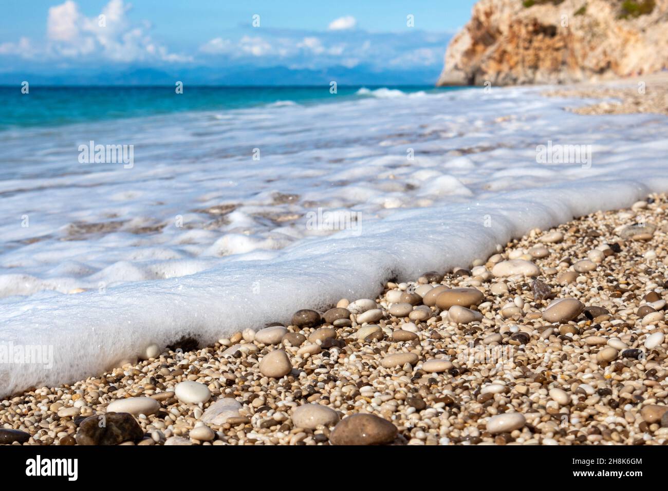 Playa de guijarros Mylos con mar azul, espuma blanca y acantilado rocoso en la costa de la isla Lefkada en Grecia. Vacaciones de verano naturaleza viaje al mar Jónico Foto de stock