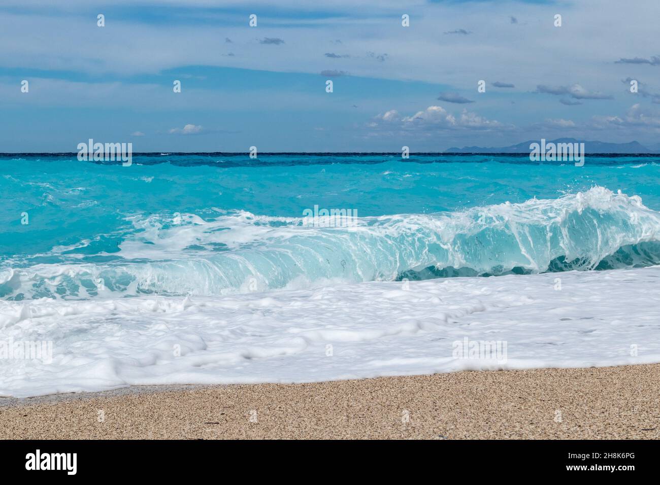 Azure vibrantes olas rompiendo en la orilla. Soleada costa de la isla griega con cielo azul. Playa de arena en Grecia. Viaje de verano por la naturaleza hasta el mar Jónico Foto de stock