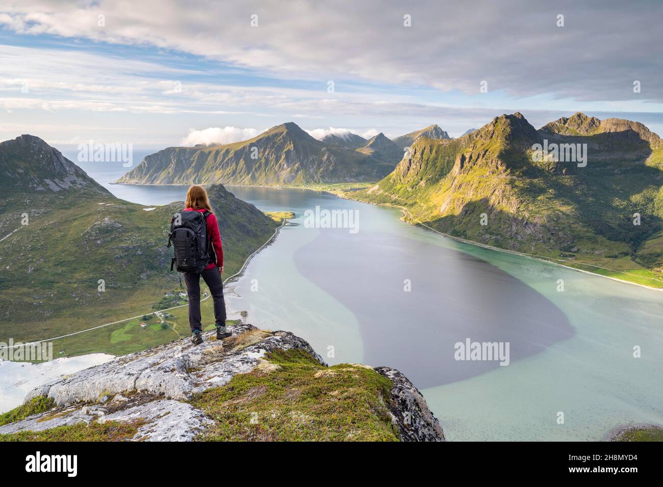 El excursionista mira desde la montaña Kollfjellet hasta el fiordo y las montañas de Lofoten, Flakstadoya, Lofoten, Noruega Foto de stock