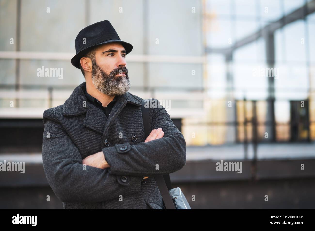 Retrato de de negocios con ropa negra frente al edificio de la empresa. El hombre con barba negra lleva ropa de invierno Fotografía de stock -