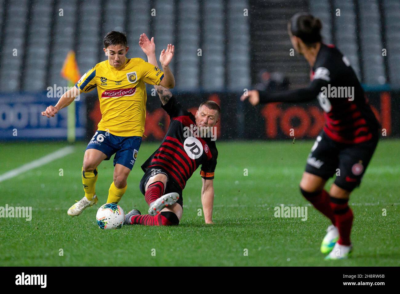 Los Wanderers del oeste de Sydney avancen hacia Mitchell Duke (7) se deslizan para enfrentarse al centrocampista Joshua Nisbet de Central Coast Mariners (26) Foto de stock