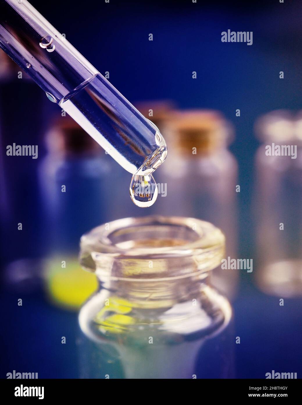gota de líquido de una pipeta en un frasco médico, concepto de investigación, nuevos fármacos y ciencia, sobre un fondo rosa, azul y morado brillante. Foto de stock