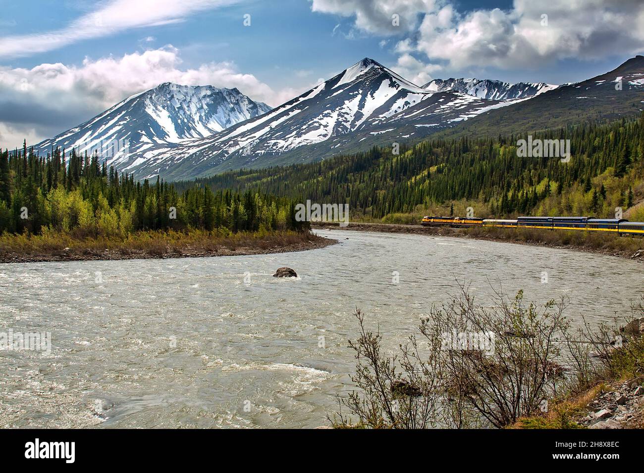 Tren cruzando la frontera de Alaska, pasando por picos montañosos y ríos que fluyen. Foto de stock