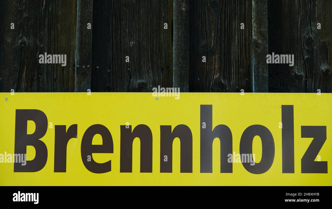 Signo amarillo que lee Leña ( traducción de la palabra alemana Brennholz: Leña ). En la pared de madera marrón de fondo, Alemania. Foto de stock