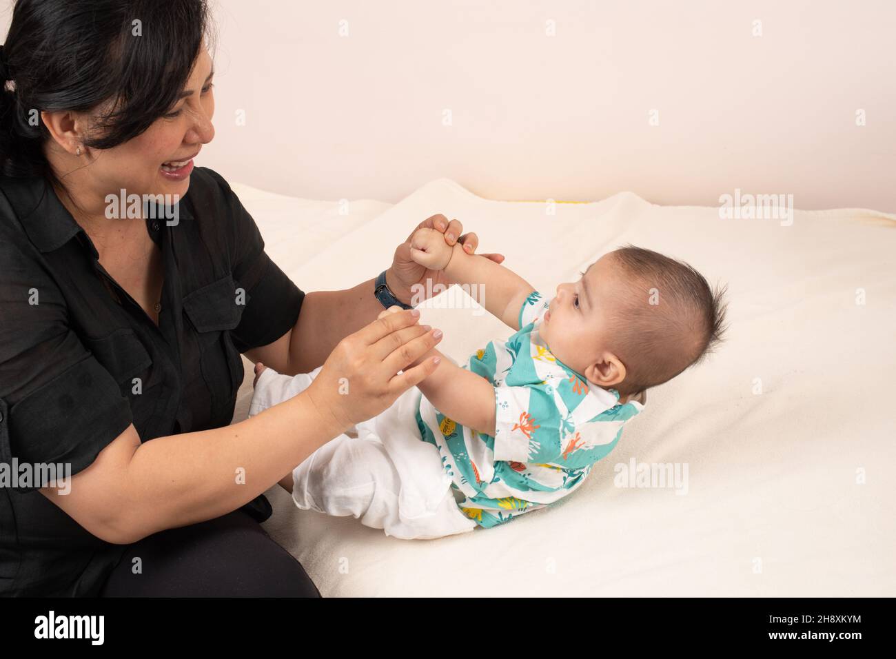 niño de 3 meses con madre, tirado a la posición sentada mientras ella lo tira de sus manos Foto de stock
