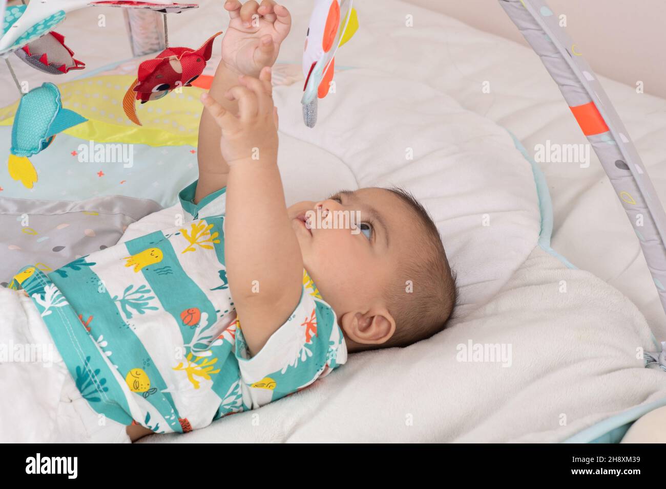 niño de 3 meses de edad en la parte de atrás de la mano para los juguetes colgando de la barra de juguetes Foto de stock