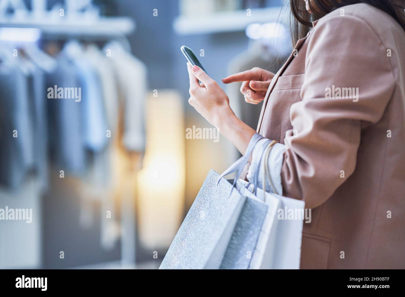 Mujer agradable con teléfono en la tienda de ropa Foto de stock