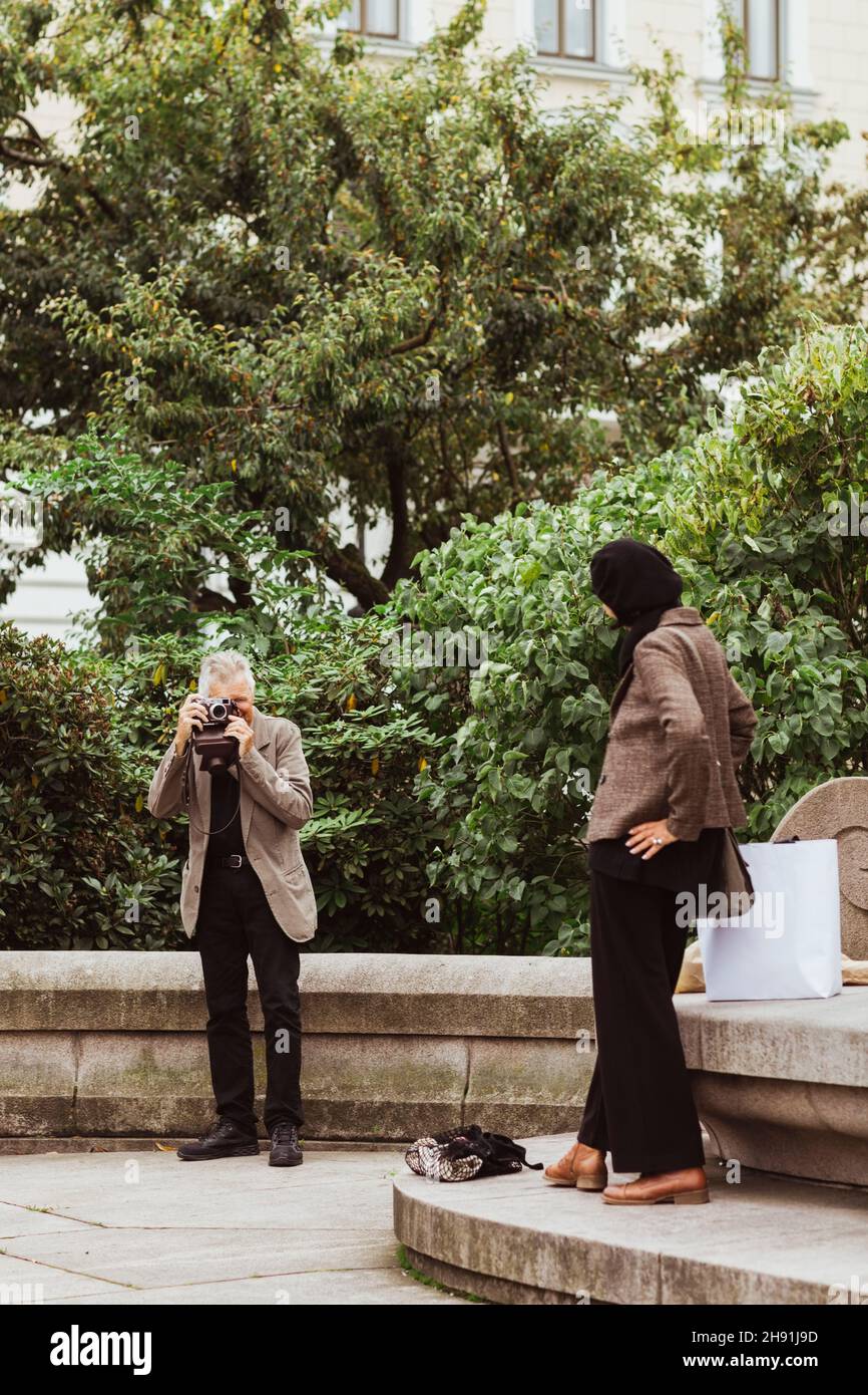 Hombre mayor fotografiando a una mujer de pie en el parque durante el fin de semana Foto de stock