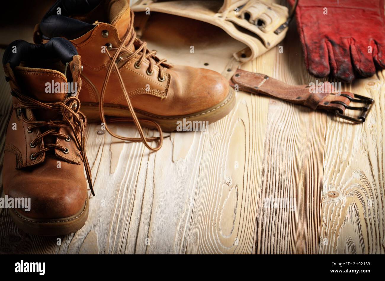 Cuero amarillo usado botas de trabajo con cinturón de herramientas y guantes protectores de madera en primer plano de fondo. Lugar para el texto Foto de stock