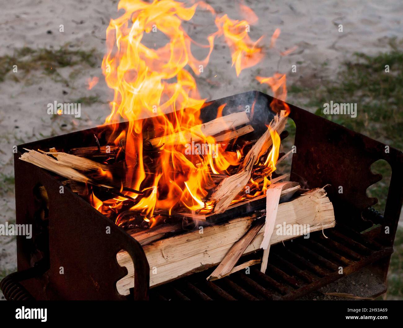 Troncos de madera quemados en un pequeño fuego construido sobre una parrilla de camping Foto de stock