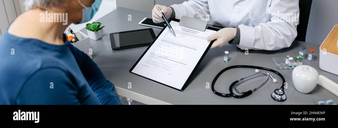 El médico le explica a su paciente el formulario de consentimiento para la vacuna contra el coronavirus Foto de stock