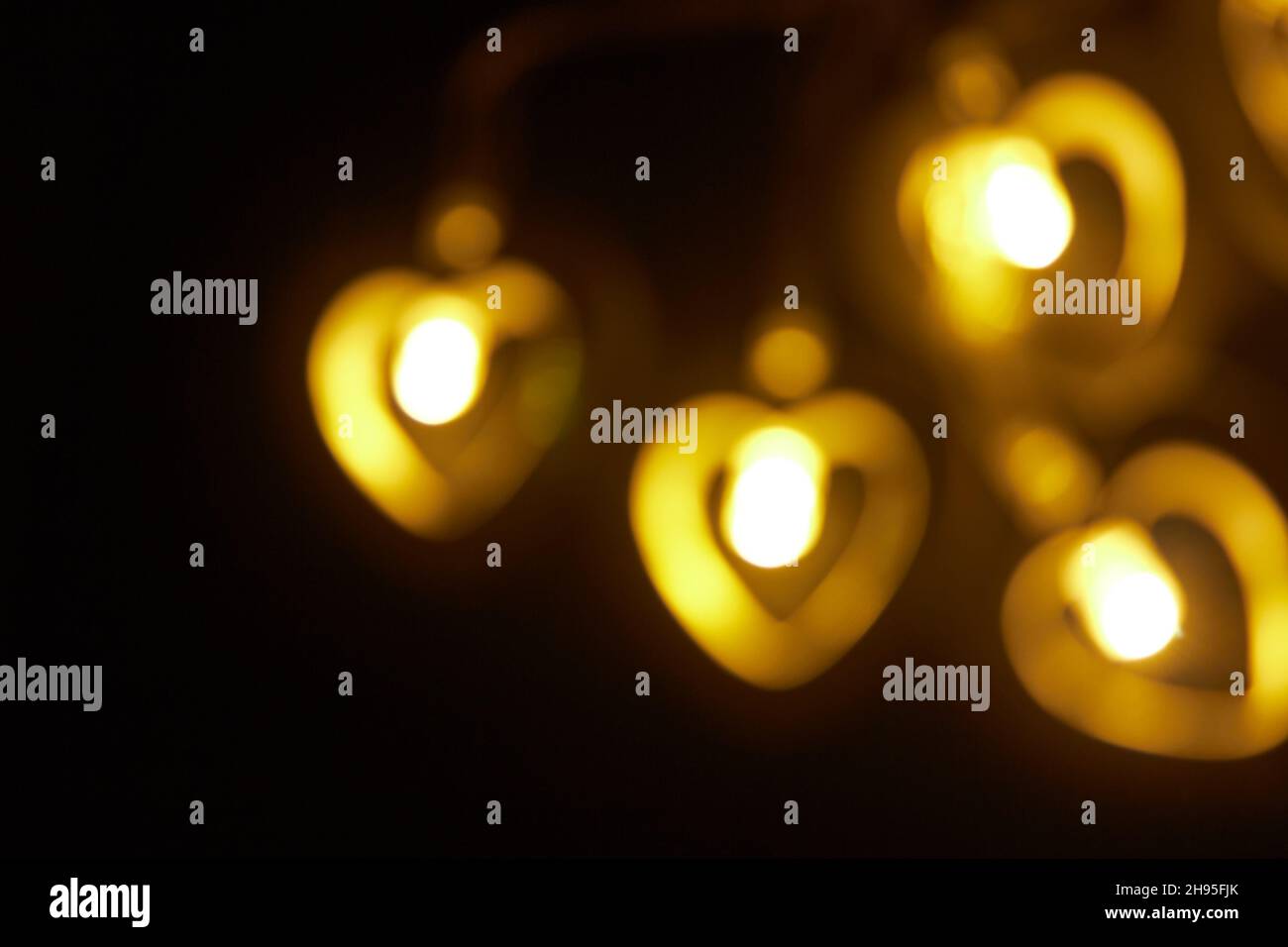 Cuatro grandes luces borrosas doradas en forma de corazón sobre un fondo negro. Fondo de pantalla grande amarillo abstracto borroso para Navidad, tema de amor, San Valentín Foto de stock