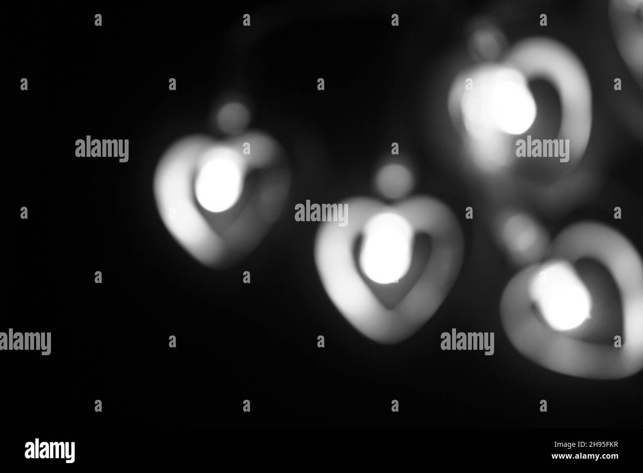 Cuatro grandes luces blancas y grises borrosas en forma de corazón sobre un fondo negro. Fondo de pantalla grande abstracto borroso para Navidad, tema de amor, Valentin Foto de stock