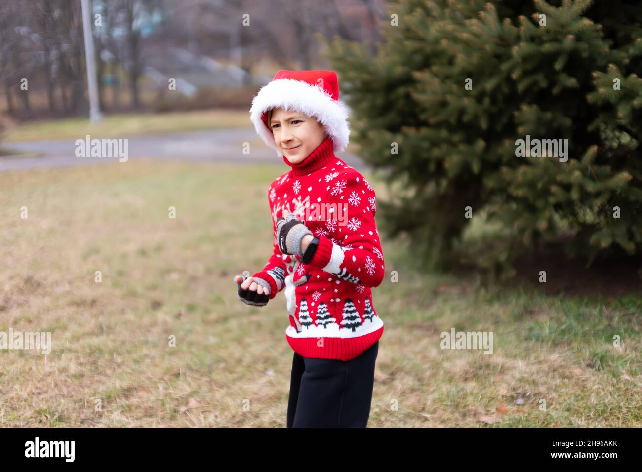 Un niño en un cálido suéter de Navidad con un ciervo de Año Nuevo y un sombrero de Santa muestra su pecho con sus manos y muecas Foto de stock