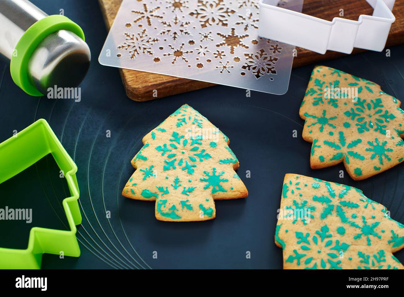 Galletas con forma de árbol de Navidad con patrón de copos de nieve, plantilla, cortadores de galletas, pasador rodante, tabla de cortar en una alfombrilla para hornear Foto de stock